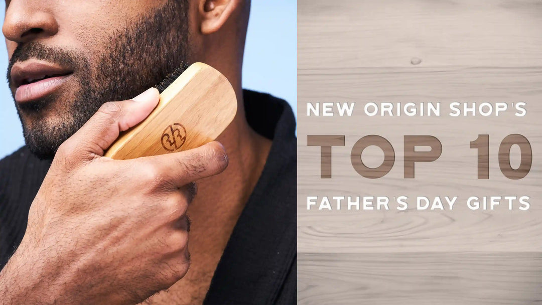 A black man holding a beard brush up to his beard. The right side of the image is a wood texture with the words "New Origin Shop's Top 10 Father's Day Gifts"