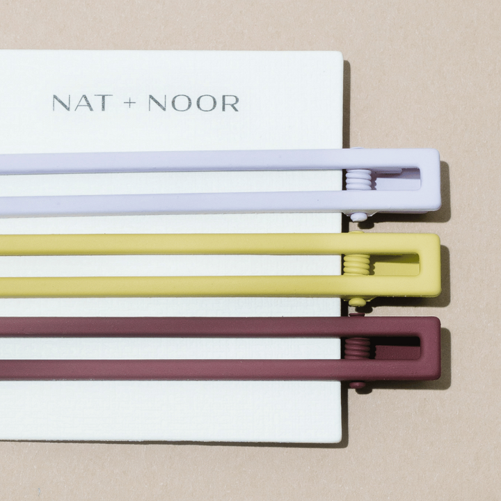 NAT+NOOR set of three hairclips, one white, one yellow, one brown, on a white card on a tan background