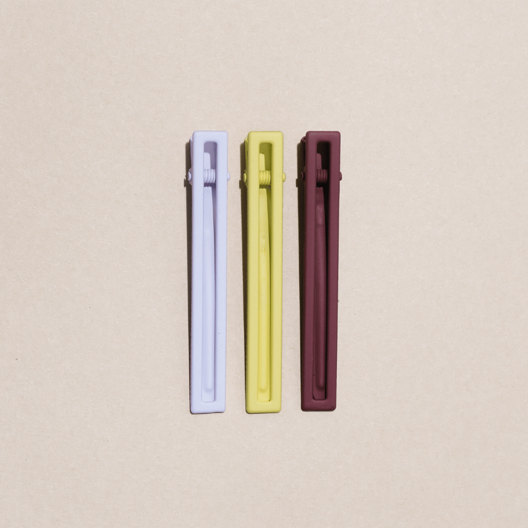 a set of three hairclips, one white, one yellow, one brown, on a tan background