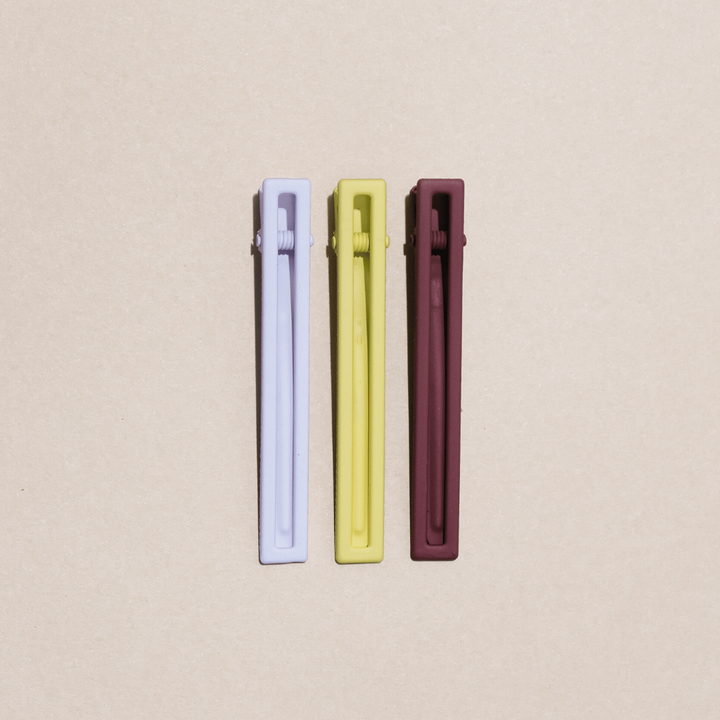 a set of three hairclips, one white, one yellow, one brown, on a tan background