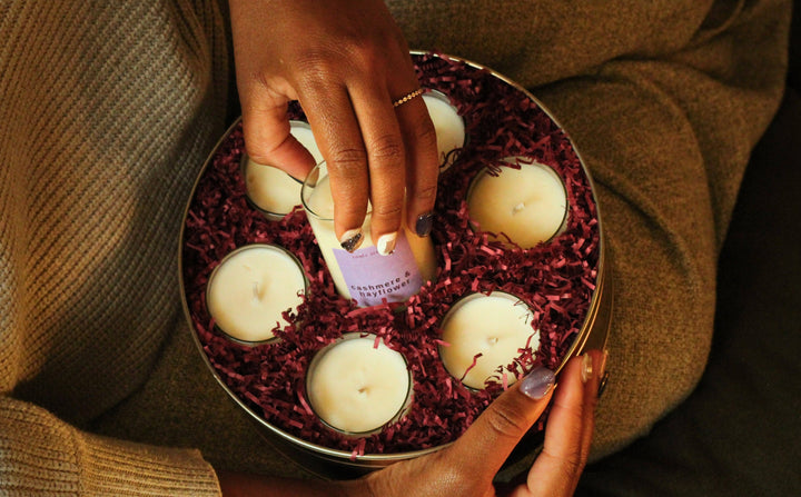 Person holding a round container with candles and a purple item, wearing a gold ring.