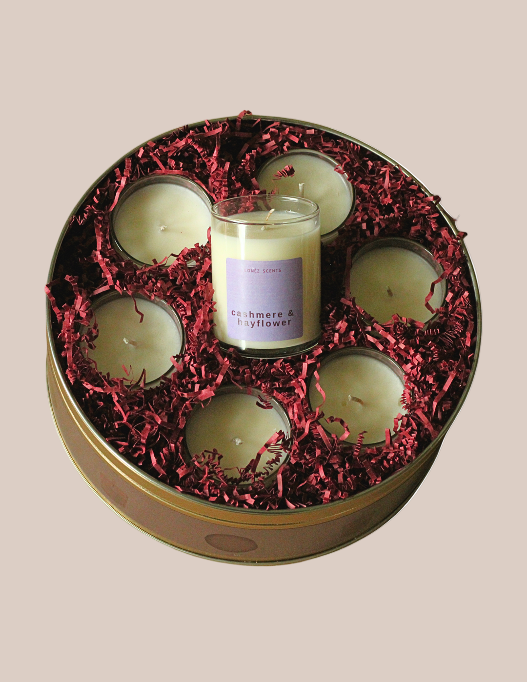 Set of candles in a round tin with red shredded paper on a beige background