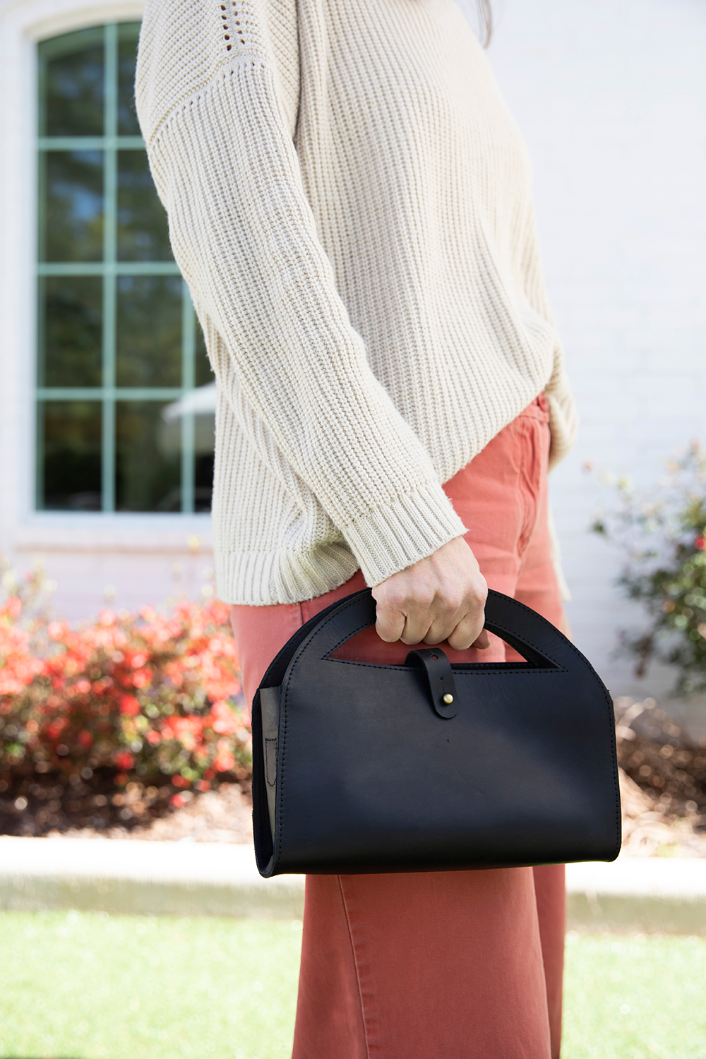Person holding a black handbag outdoors with a blurred background