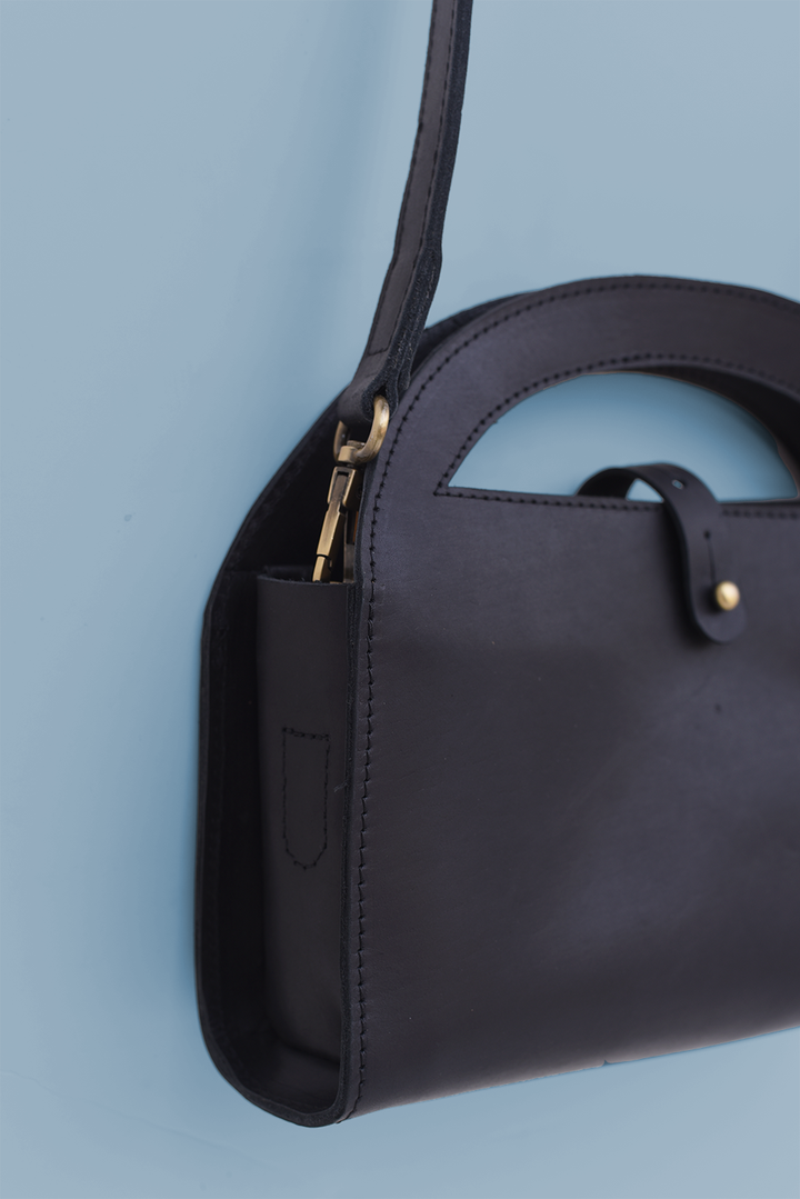 Black handbag with a gold zipper on a light blue background