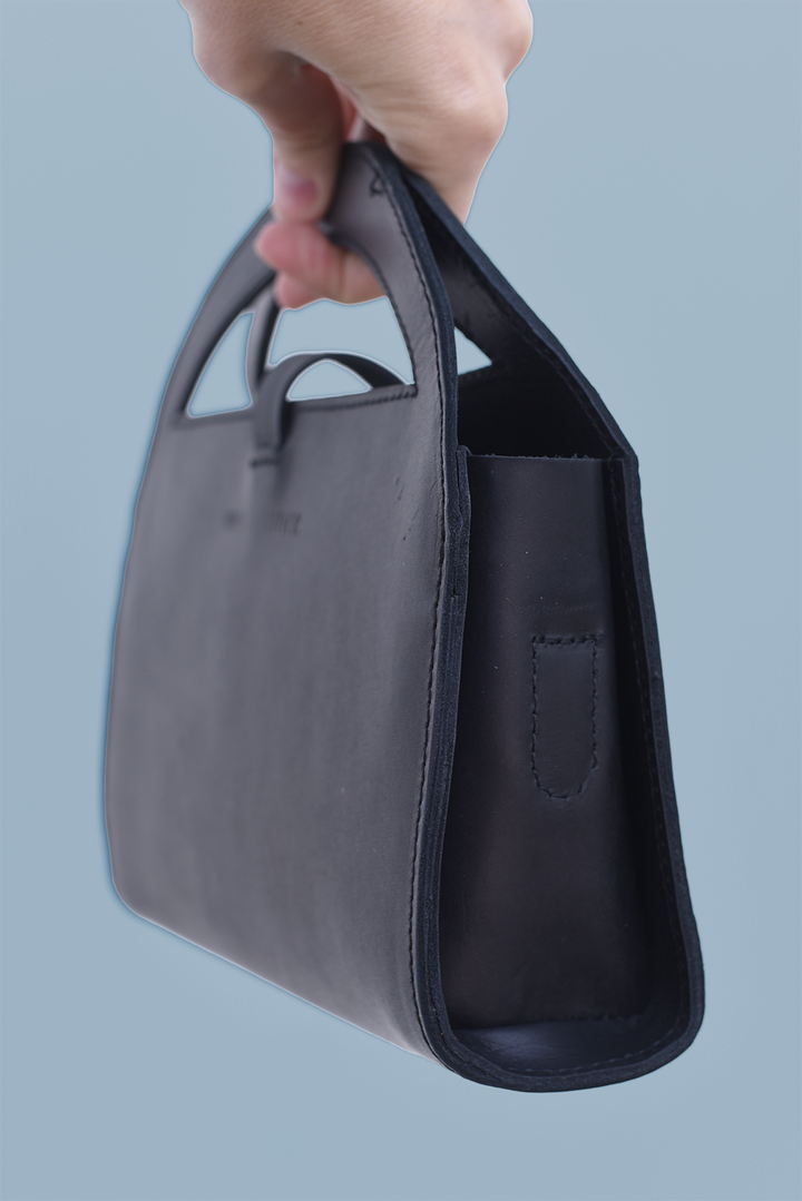 Hand holding a dark gray handbag against a light blue background