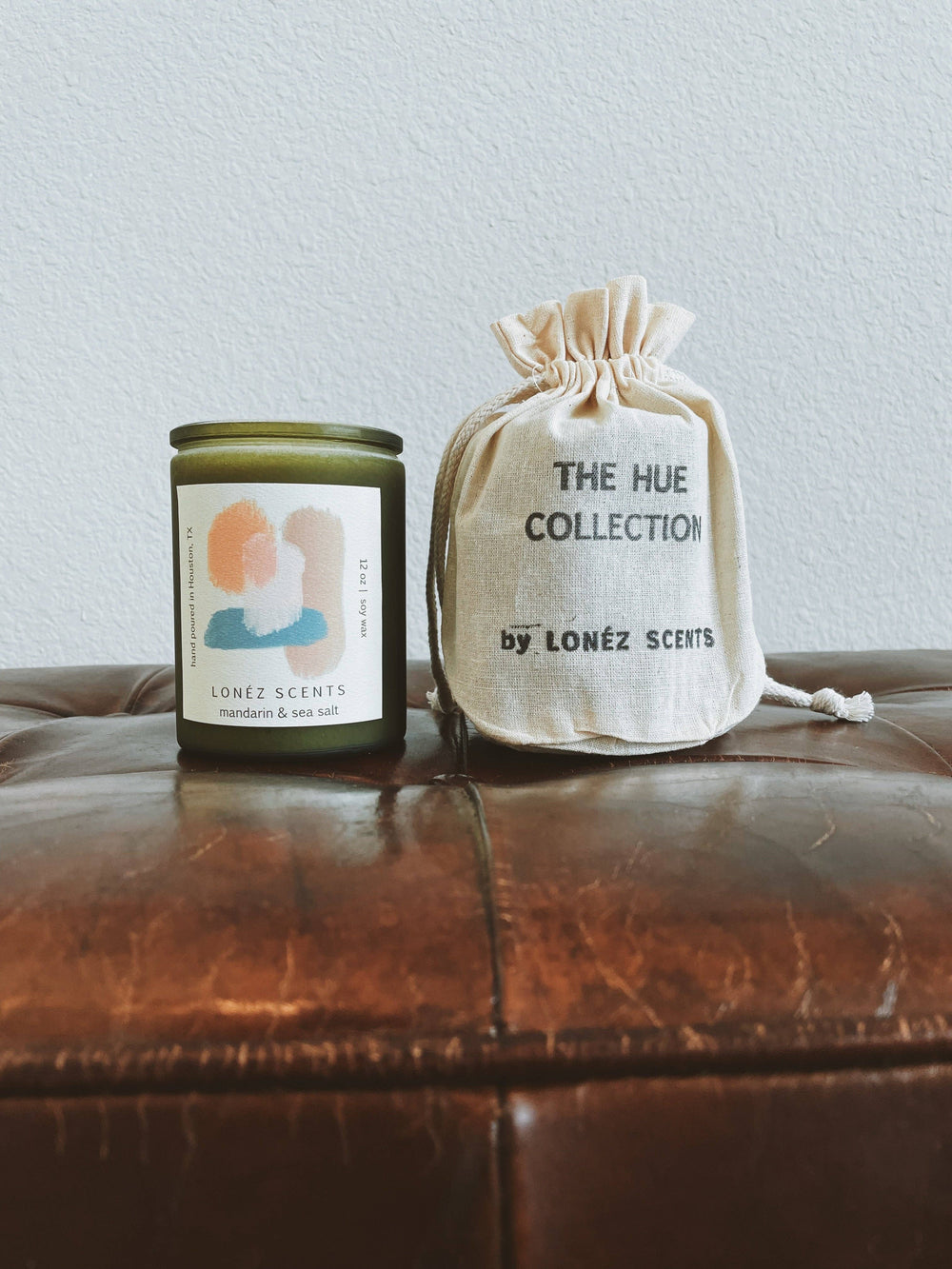 Candle and drawstring bag from The Hue Collection by LONEZ SCENTS on a leather surface.