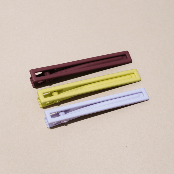 A set of three hair clips in different colors lying on a beige surface.