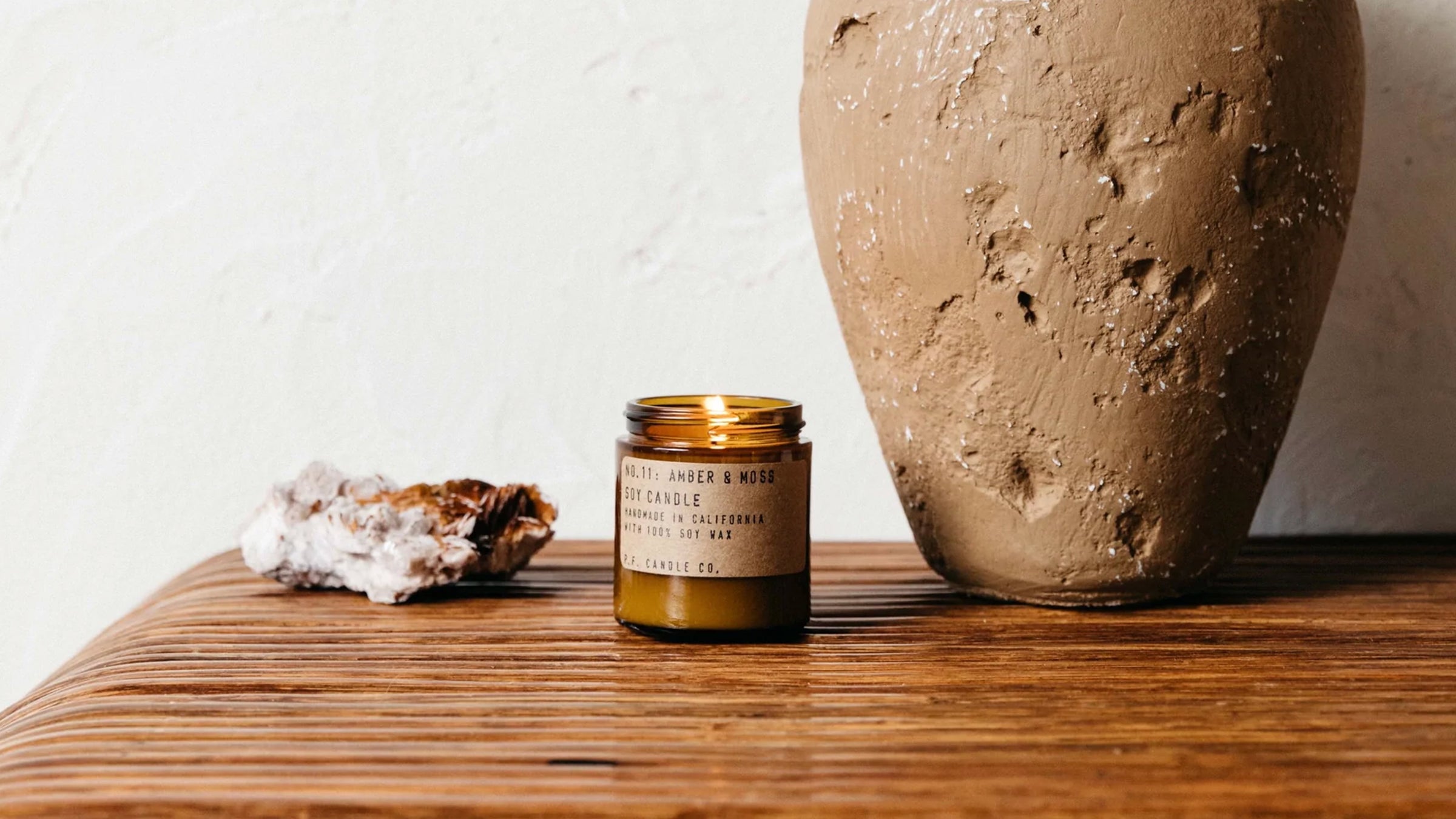 P F Candle Co candle on dresser top next to a stone vase and crystal