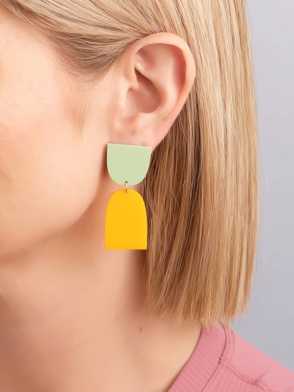 Yellow and green earrings worn by a person with a neutral background