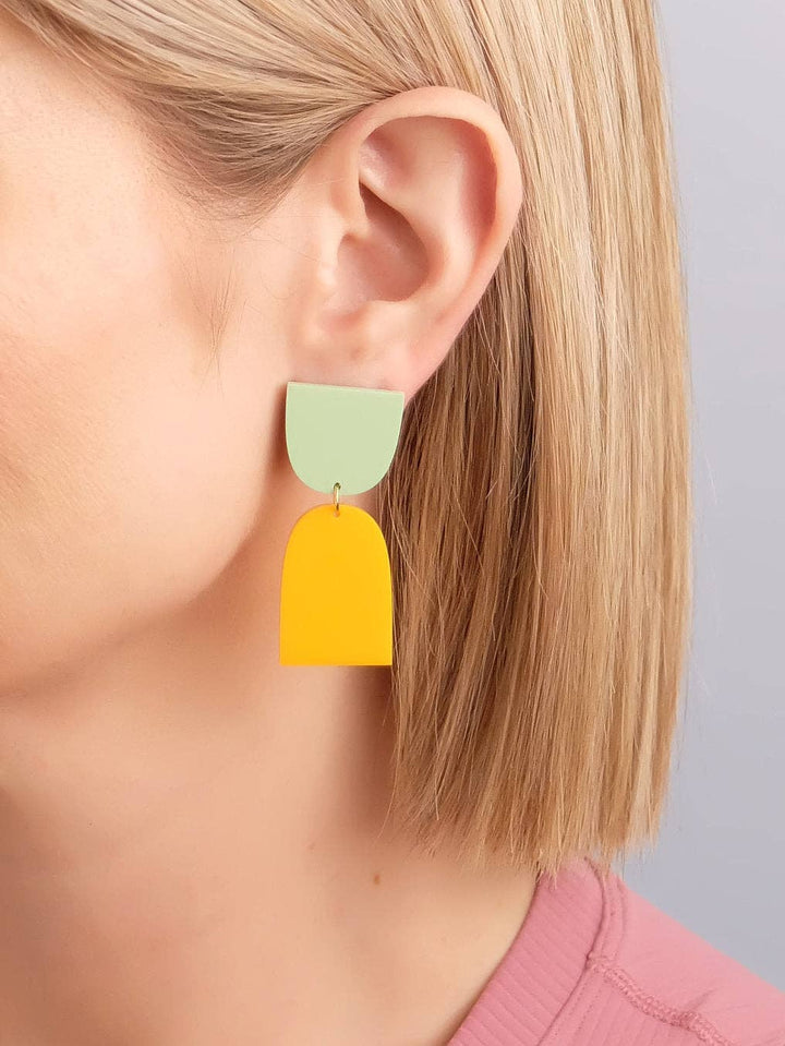 Yellow and green earrings worn by a person with a neutral background