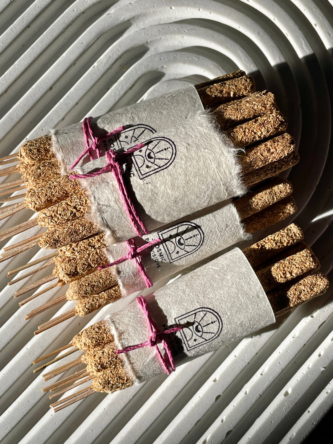 Hand-rolled Palo Santo incense sticks tied with pink string, packaged in sets on a textured surface.