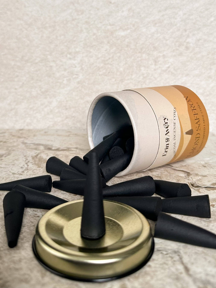 Black incense with a gold lid spilling out of an open cardboard tube on a textured surface.