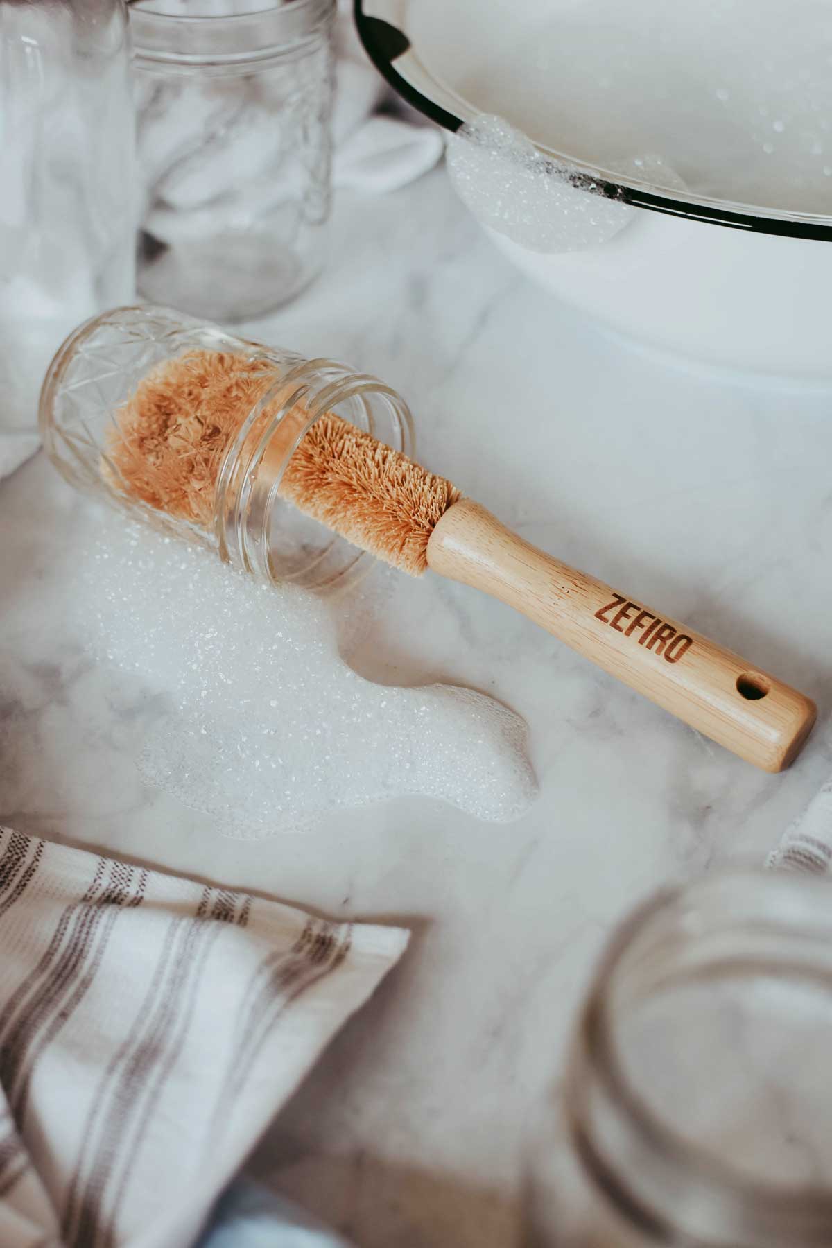 Bristle brush with wooden handle labeled 'Zefiro' on a marble surface with jars and a towel.