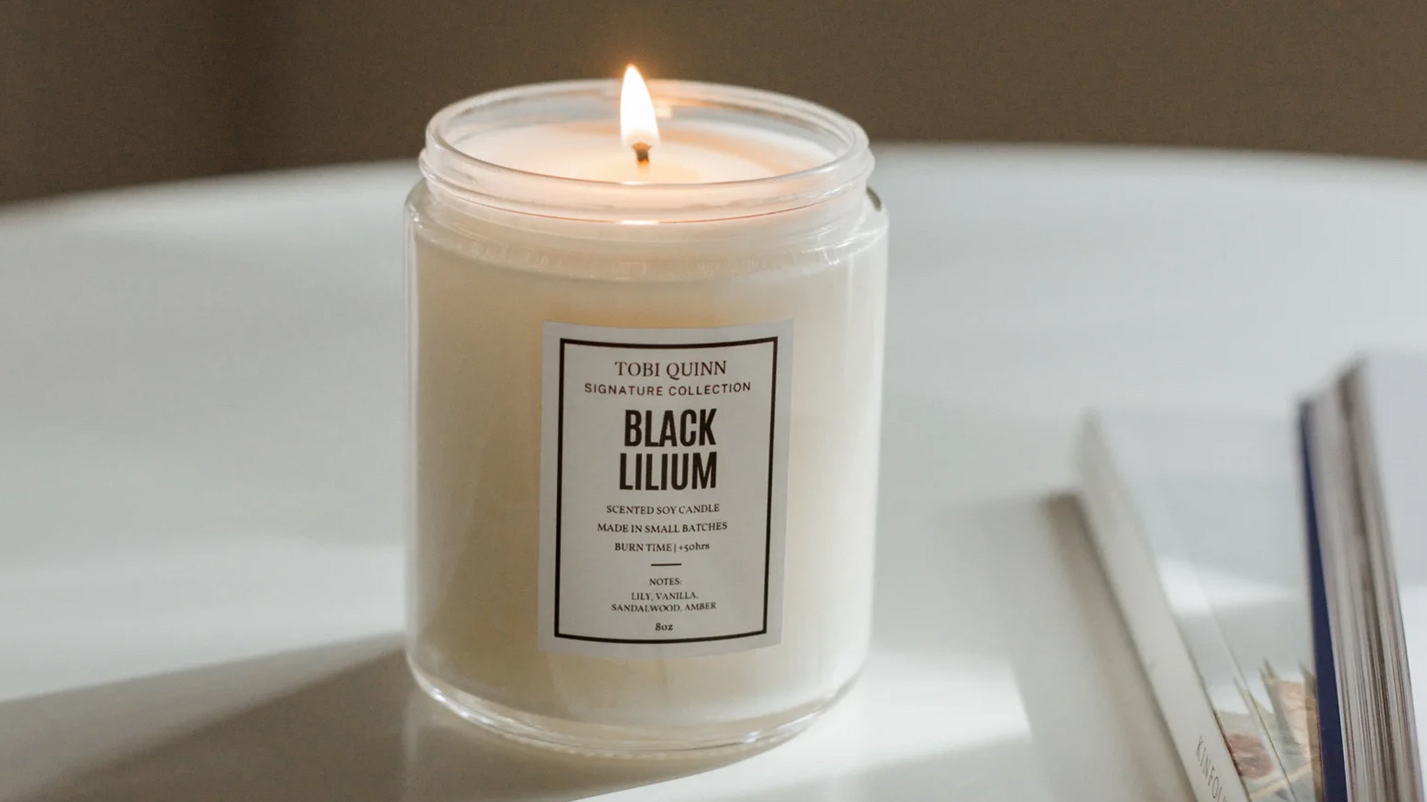 A lit Tobi Quinn Black Lilium candle on a table top