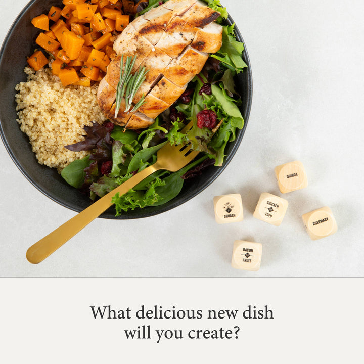 Bowl of salad with chicken, quinoa, and roasted vegetables on a white surface with decorative dice.