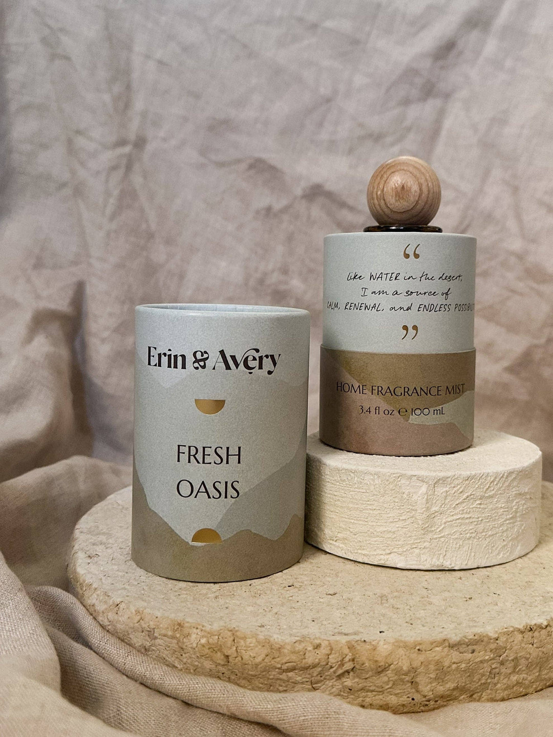 Erin &amp; Avery Fresh Oasis home fragrance mist in a white and beige cylindrical tin, displayed next to its wooden diffuser cap on a rustic stone pedestal.