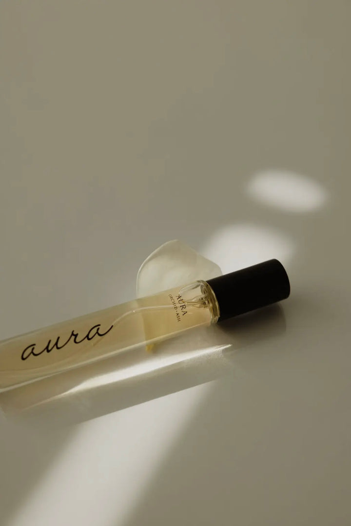 Perfume bottle labeled 'aura' on a reflective surface with soft lighting