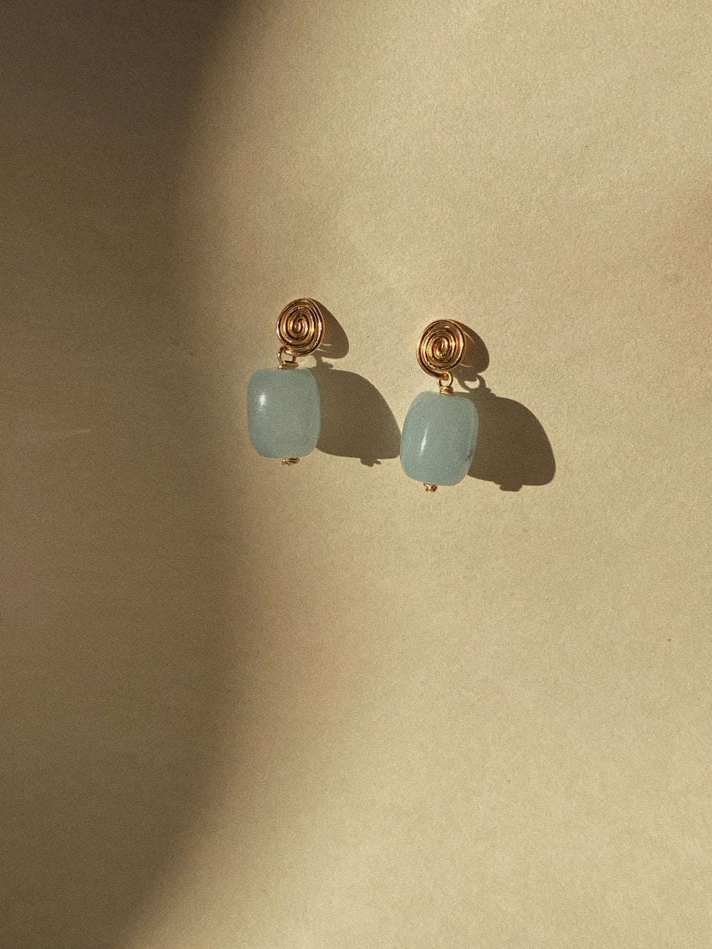 Pair of earrings with gold hooks and light blue gemstones on a beige background