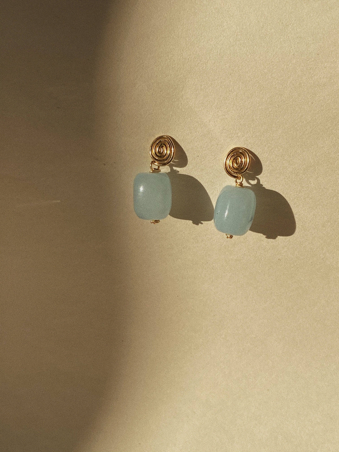 Pair of earrings with gold hooks and light blue beads on a beige background
