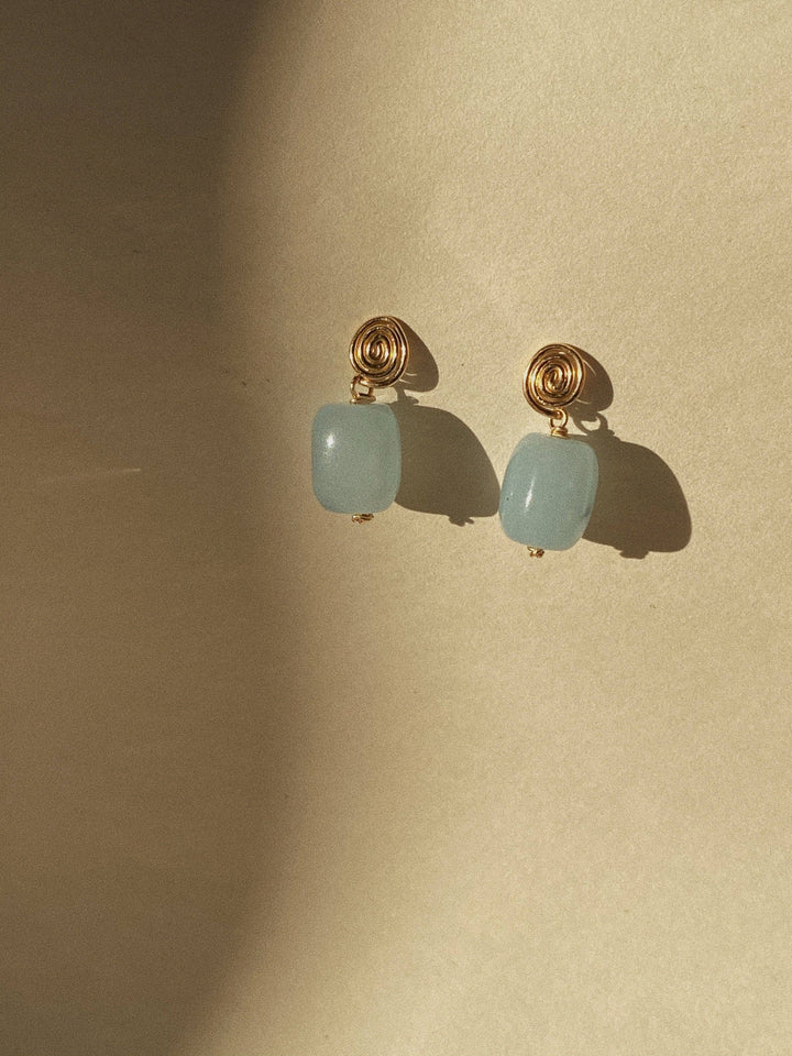 Pair of earrings with gold hooks and light blue beads on a beige background