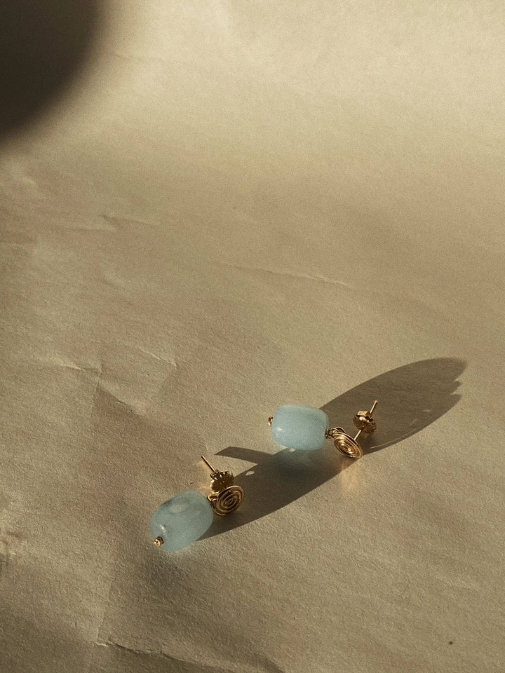 Pair of earrings with blue beads and gold posts on a beige surface