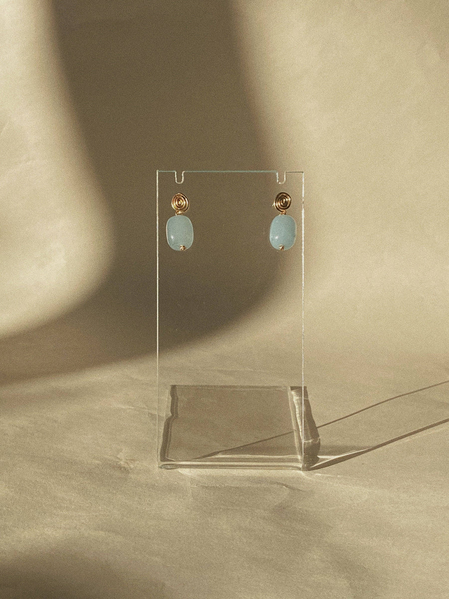 Pair of earrings on a clear stand against a beige background