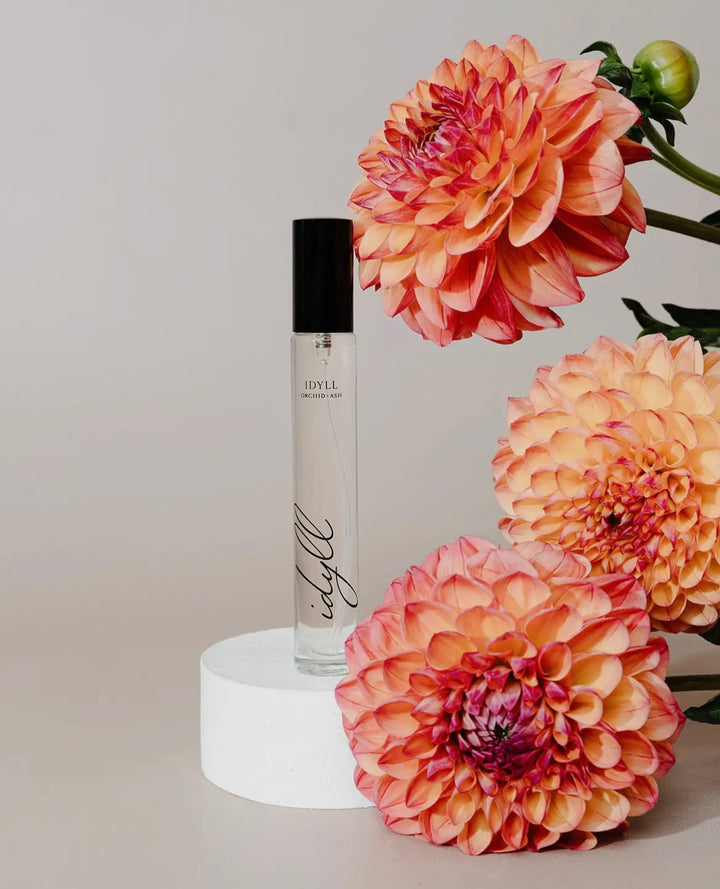 Perfume bottle on a white pedestal with pink flowers in the background