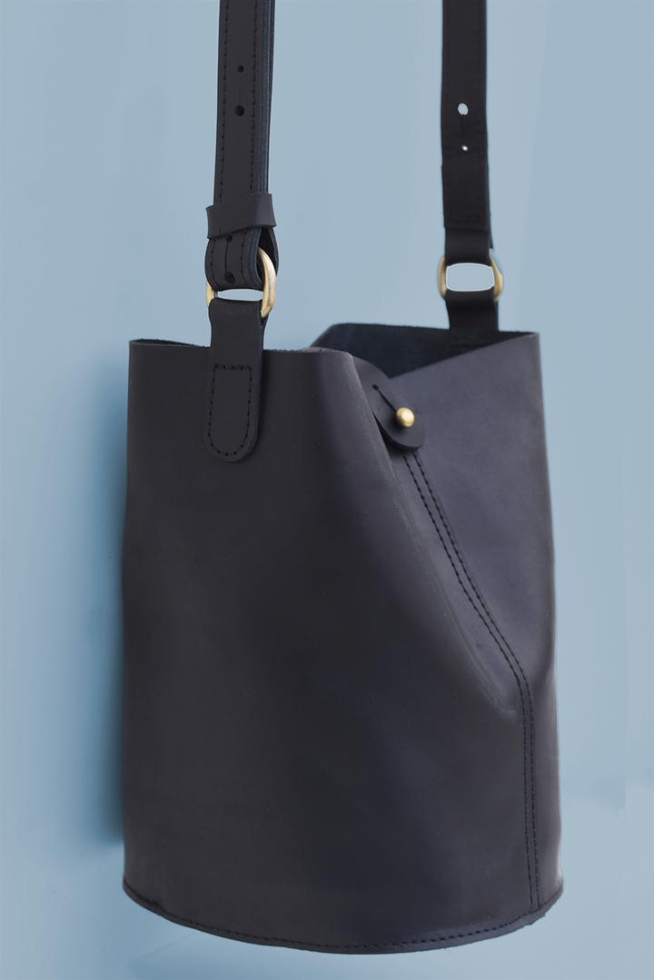 Black leather bucket bag with gold hardware on a light blue background