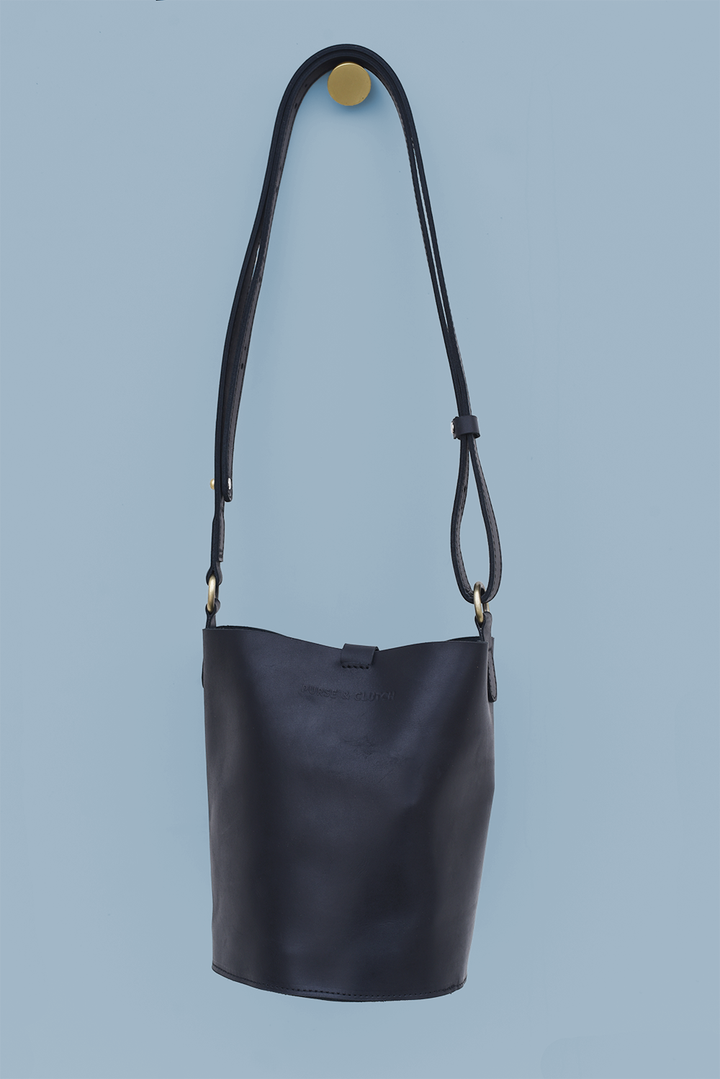 Black leather shoulder bag with a strap on a light blue background