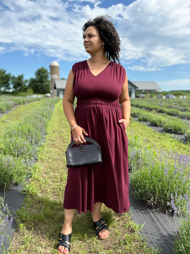 Woman in a burgundy dress standing in a lavender field with a black handbag.