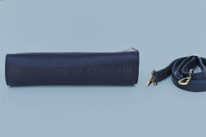 black leather bag with strap on a light blue background