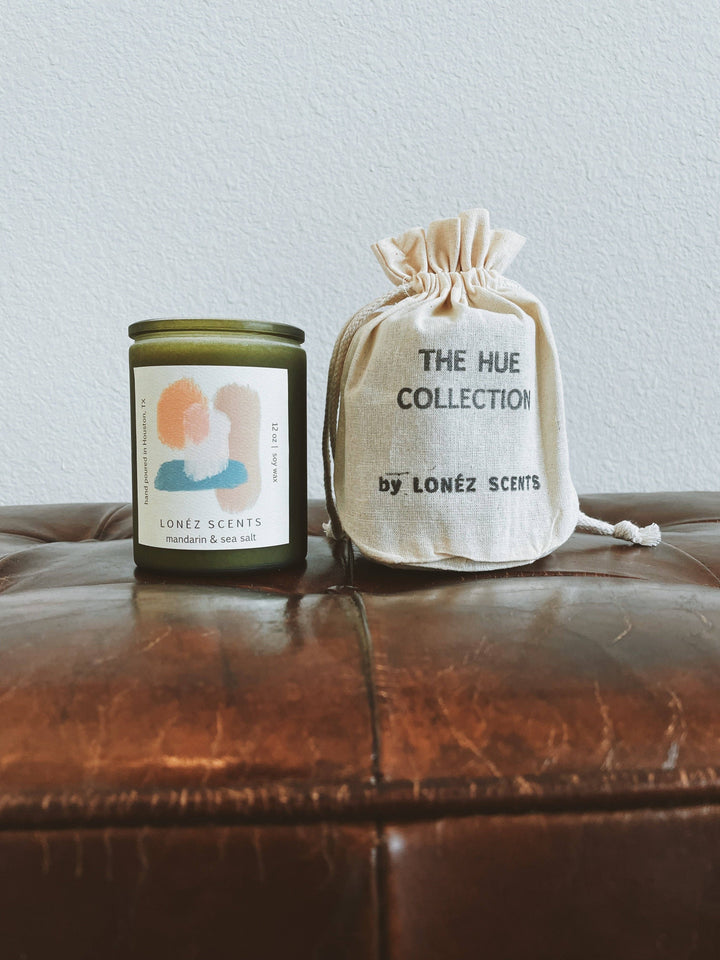 Candle and drawstring bag from The Hue Collection by LONEZ SCENTS on a leather surface.