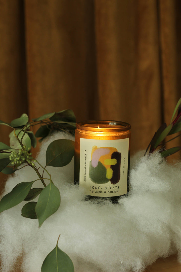 Candle with a decorative label on a white surface with green leaves