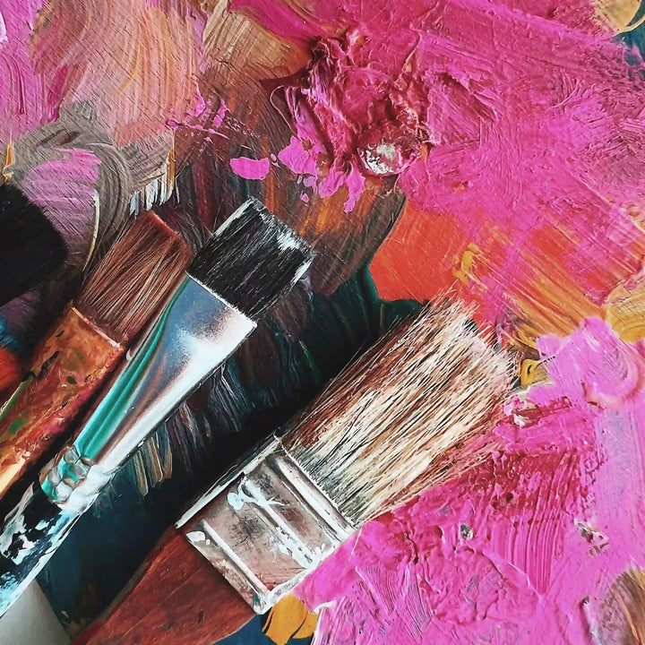 Three paint brushes on top of an abstract painting of various colors