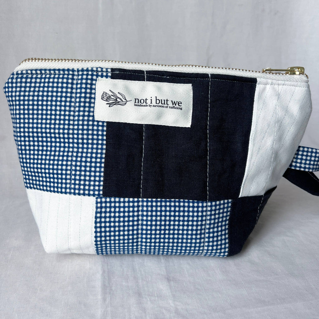 Patchwork pouch with blue and white checkered pattern and 'not i but we' label on a gray background