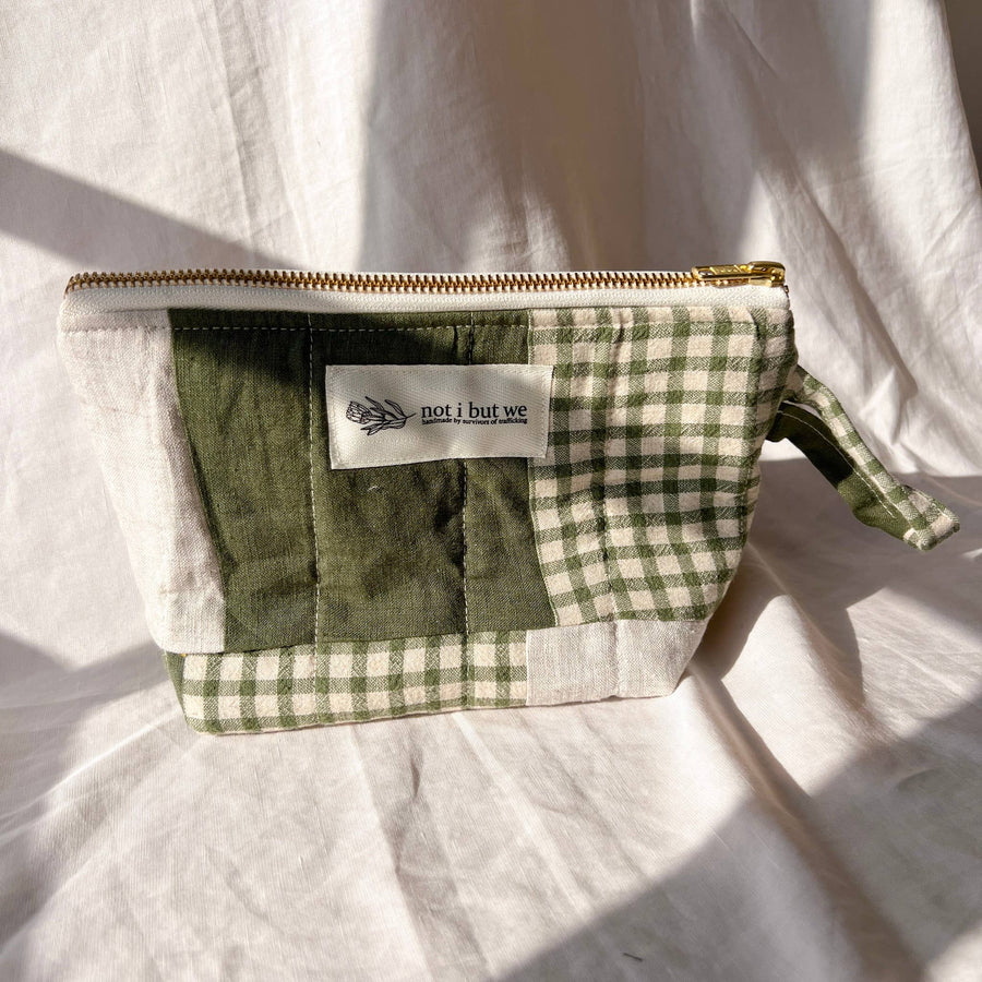Green checkered pouch with a visible brand label on a light fabric background