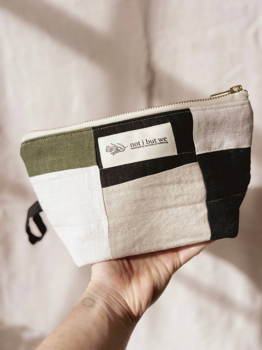 Hand holding a patchwork pouch with 'not i but we' branding against a neutral background