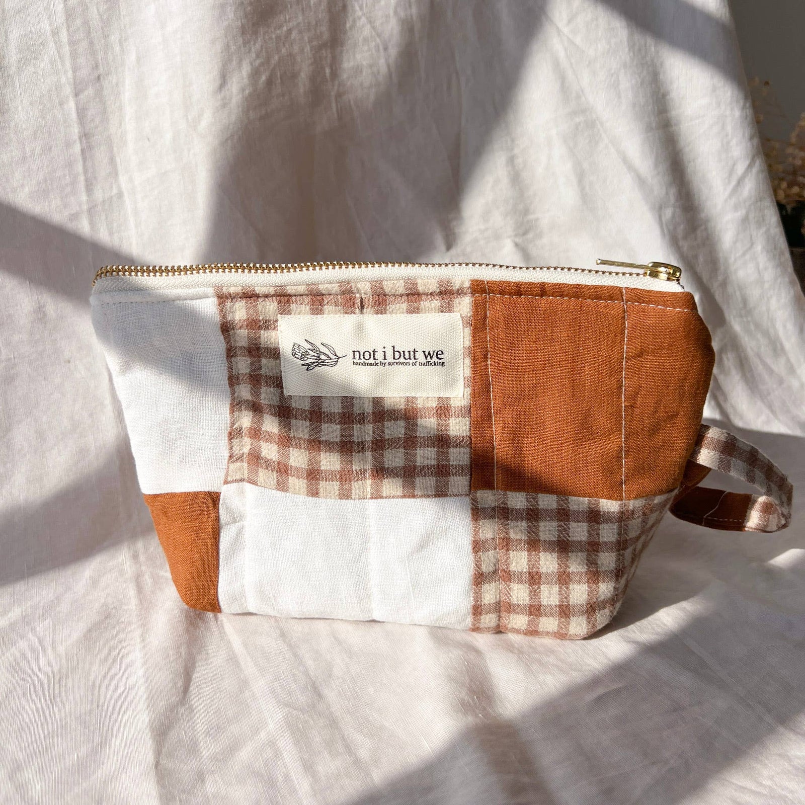 Patchwork pouch with checkered pattern and 'not i but we' label on a white fabric background