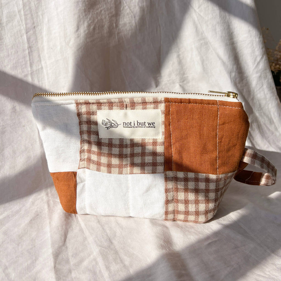 Patchwork pouch with checkered pattern and 'not i but we' label on a white fabric background