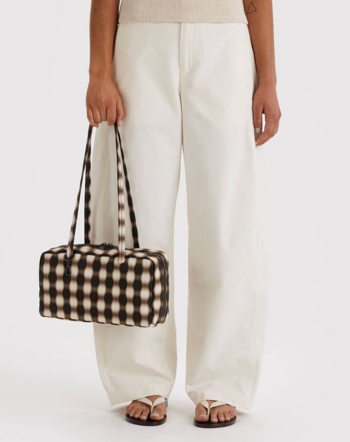 person in light top and bottoms against white backdrop holding Nylon Bowler Bag: Blurred Gingham Brown