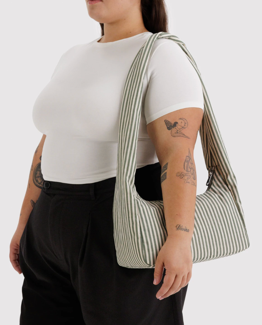 person in white top  with arm tattoos and dark bottom wearing Nylon Meringue Bag in Sage Stripeon left shoulder. white background