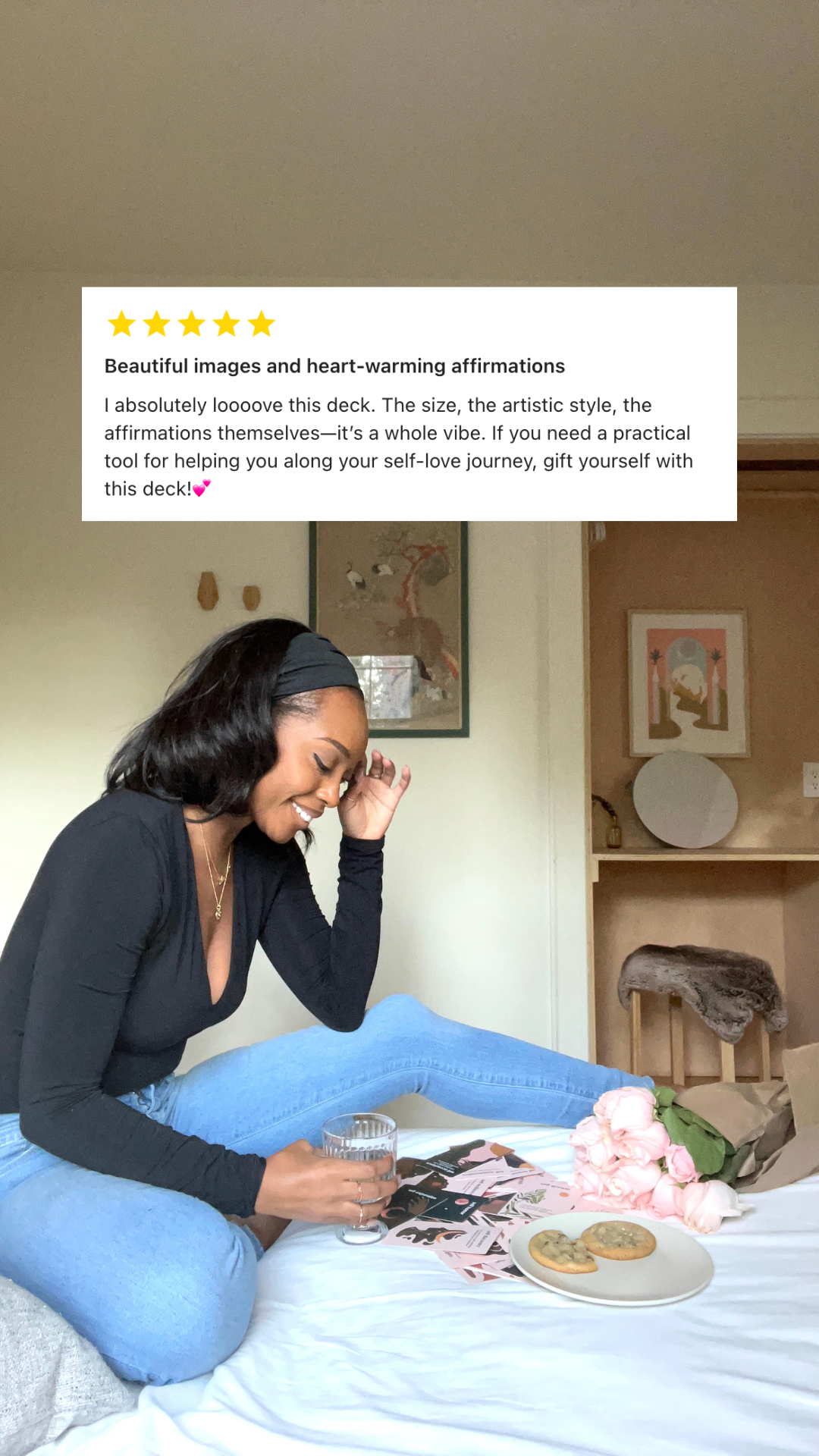 Woman sitting on a bed with a deck of cards and affirmations, surrounded by decor.