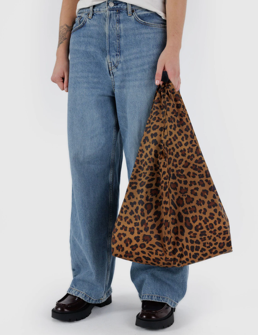person in denim and black shoes holding Standard Baggu Gradient Leopard in left hand against white background