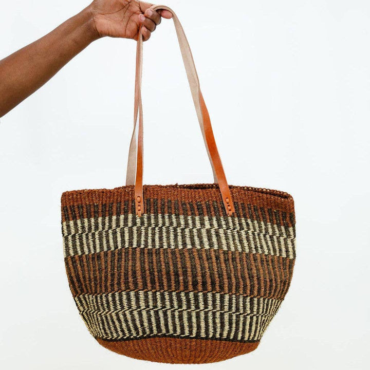 Woven basket bag with striped pattern held by a hand on a white background