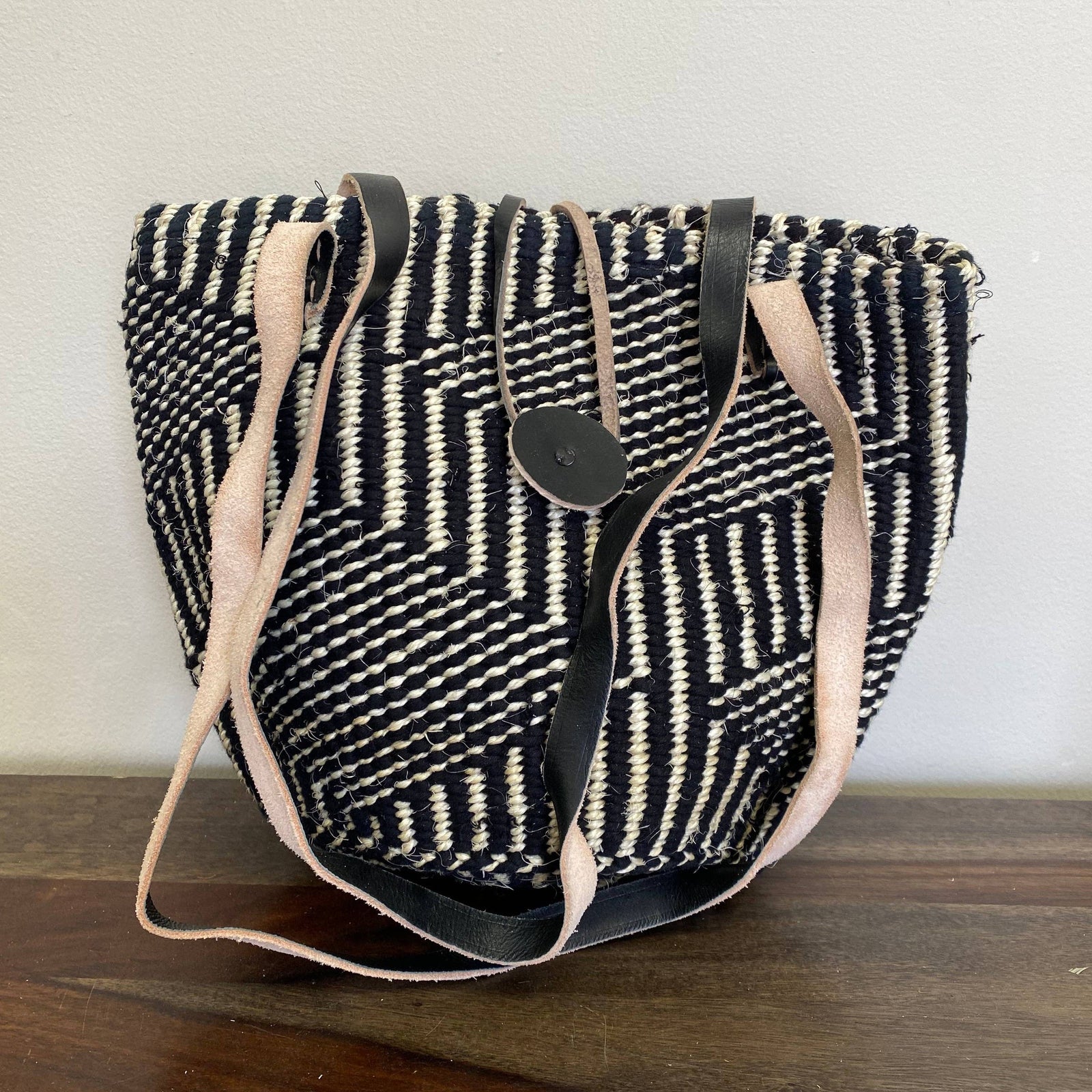 Black and white patterned bag with beige straps on a wooden surface