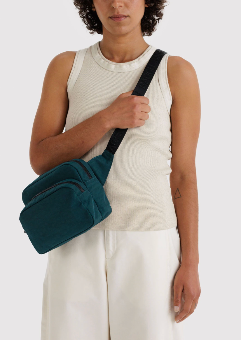 person holding baggu fanny pack in deep sea with right hand holding strap. bag across body. light top and bottom against white backdrop