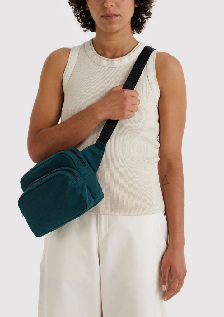 person holding baggu fanny pack in deep sea with right hand holding strap. bag across body. light top and bottom against white backdrop
