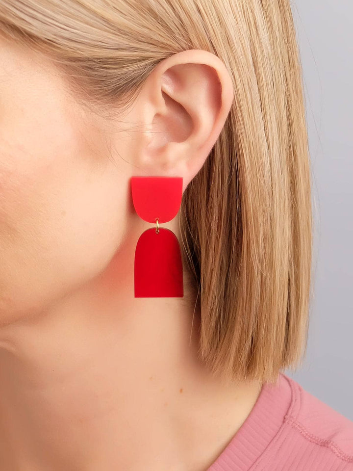 Red earrings worn by a person with blonde hair against a neutral background