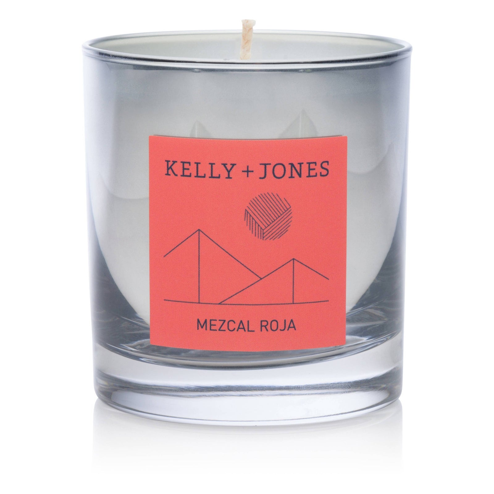 A silver painted jar candle with a pink label that reads 'KELLY + JONES MEZCAL ROJA'. The candle is depicted with a lit wick, indicating it is switchable.