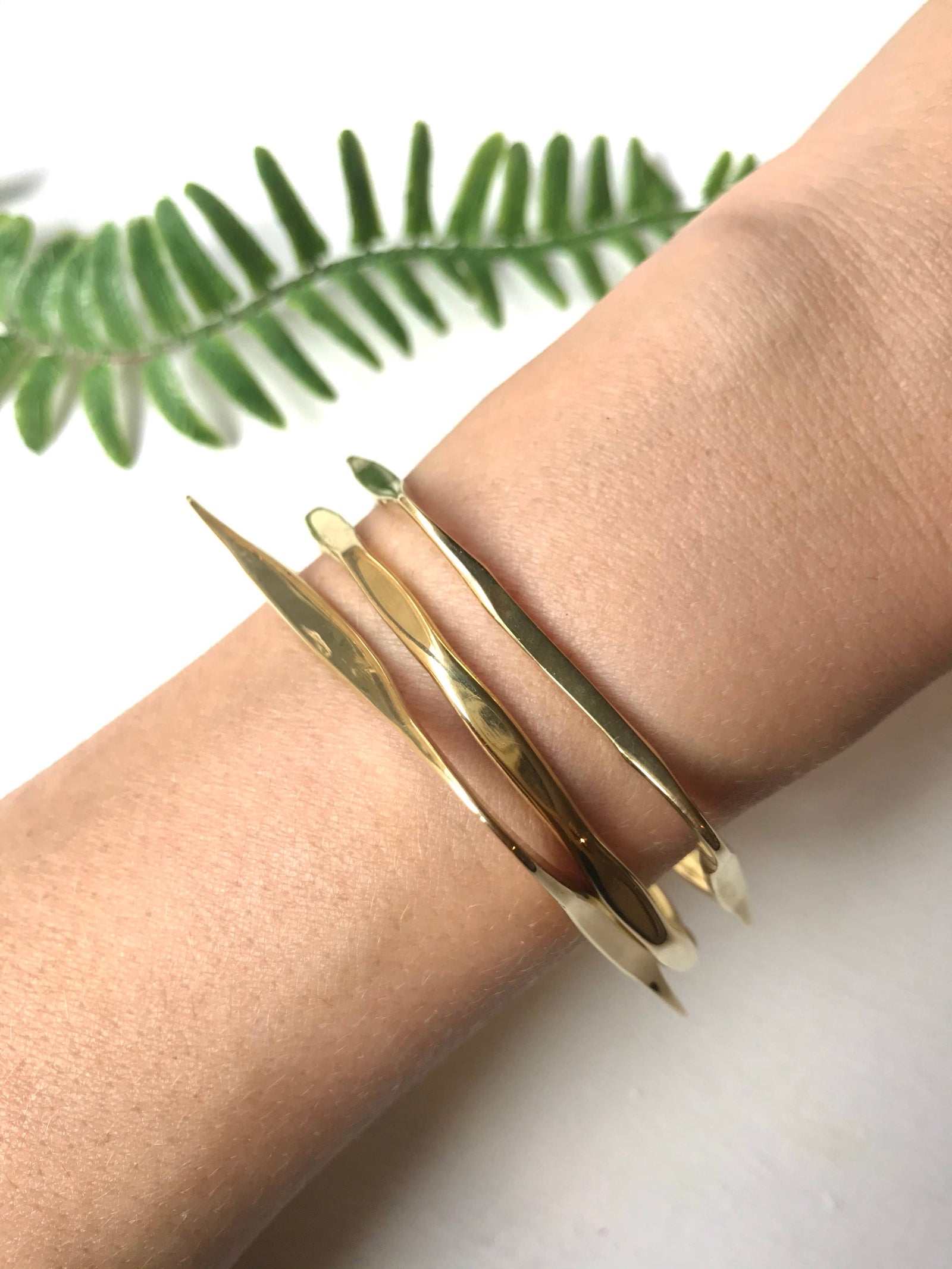 brass bracelets on a wrist with a white background and green leaves.